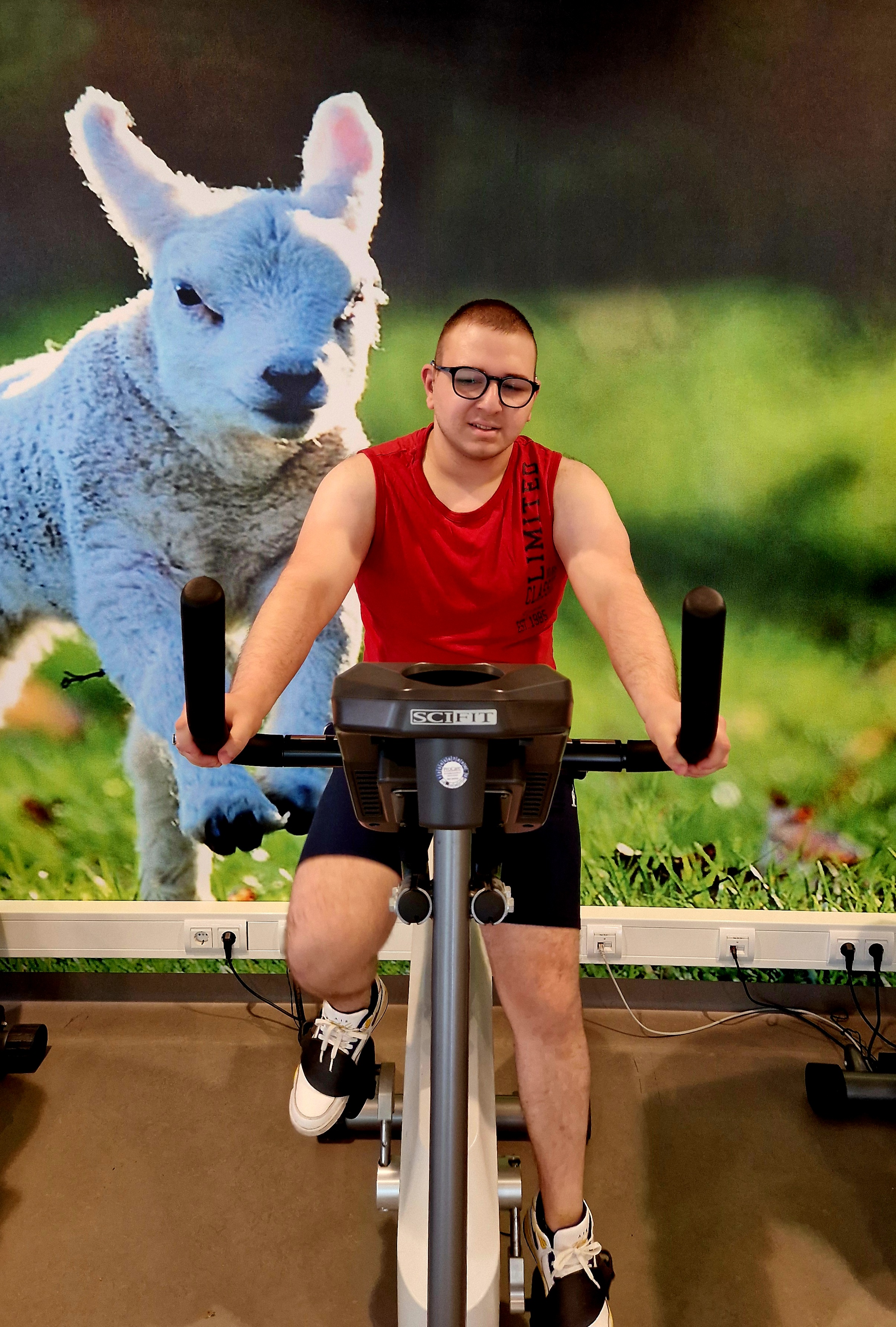 Sayfeddin op een fitnesapparaat in rood-zwarte sportkleding