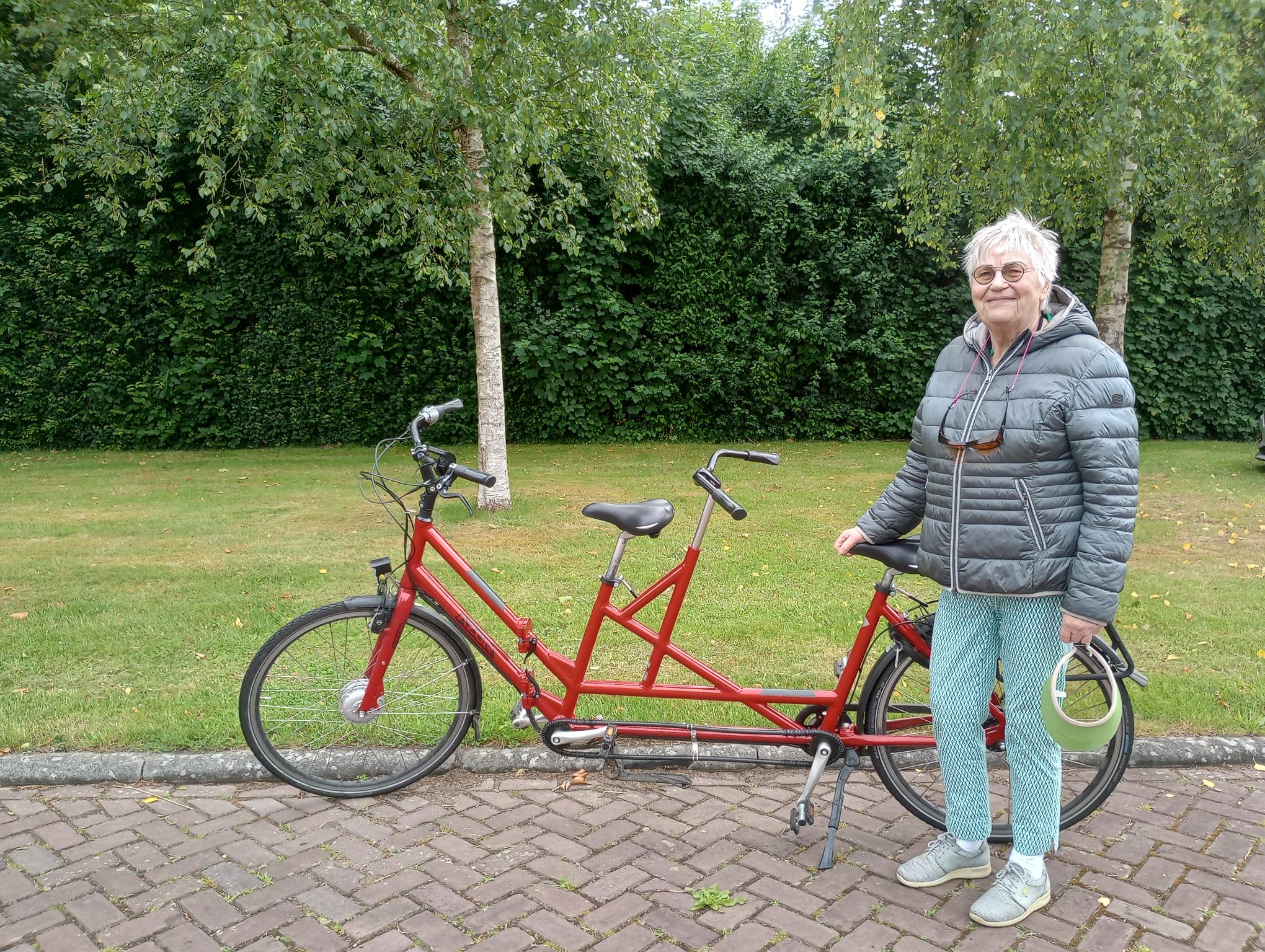 Sannie poseert lachend buiten bij een rode tandemfiets