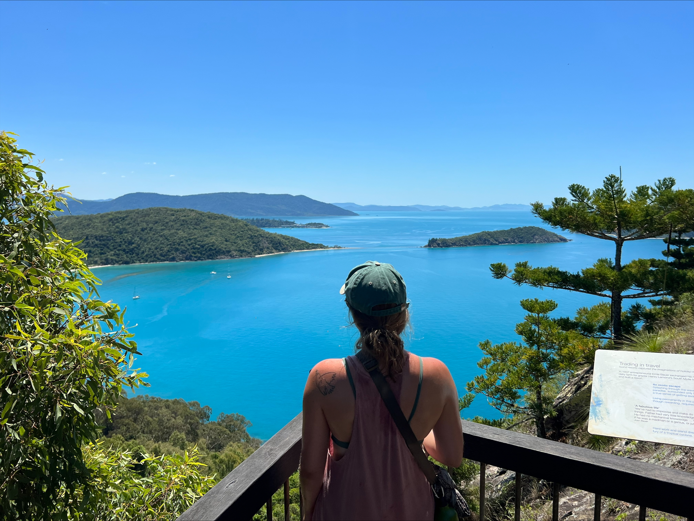 Hanna staat met haar rug naar de camera toe. Ze kijkt uit over een erg blauwe zee. Om haar heen zijn er veel planten.