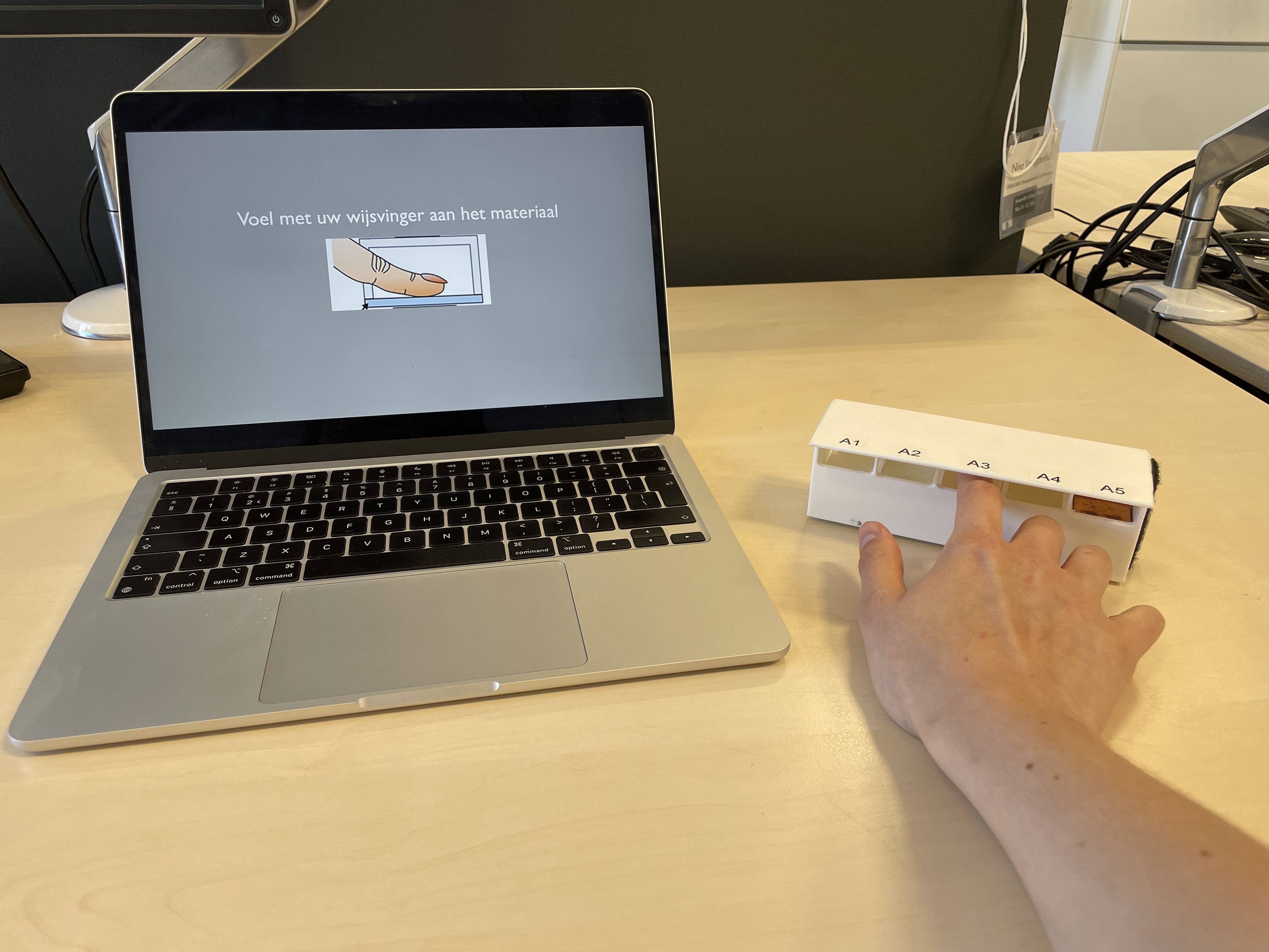 Demonstratie van iemand die materiaal voelt in het kader van het onderzoek en daarbij instructies volgt via een laptop