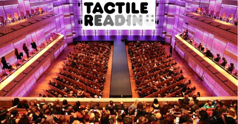 Grote zaal van het Muziekgebouw in Amsterdam gevuld met mensen. Op het beeldscherm voorin de zaal staat het logo van "Tactile Reading".