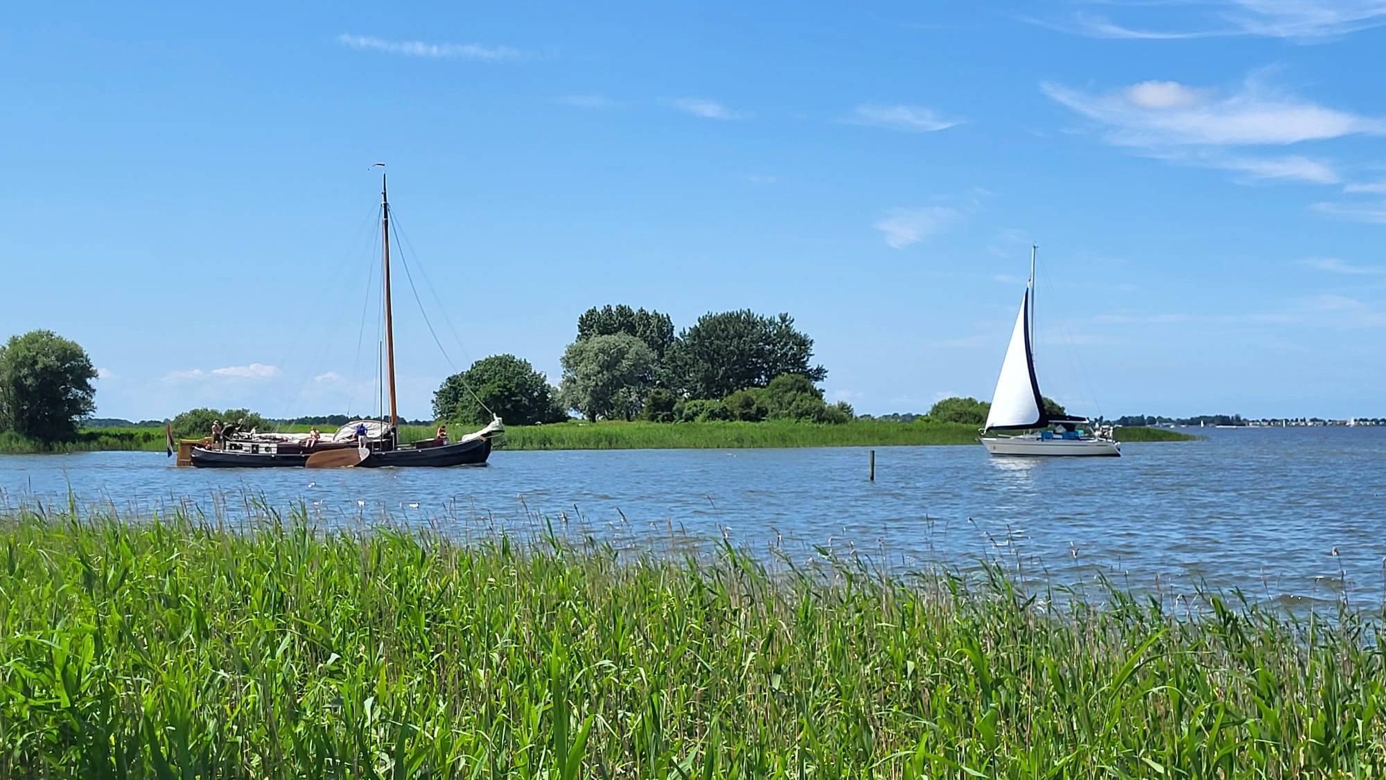Foto gemaakt vanaf het gras, kijkt uit op het water met twee boten en een heldere lucht.