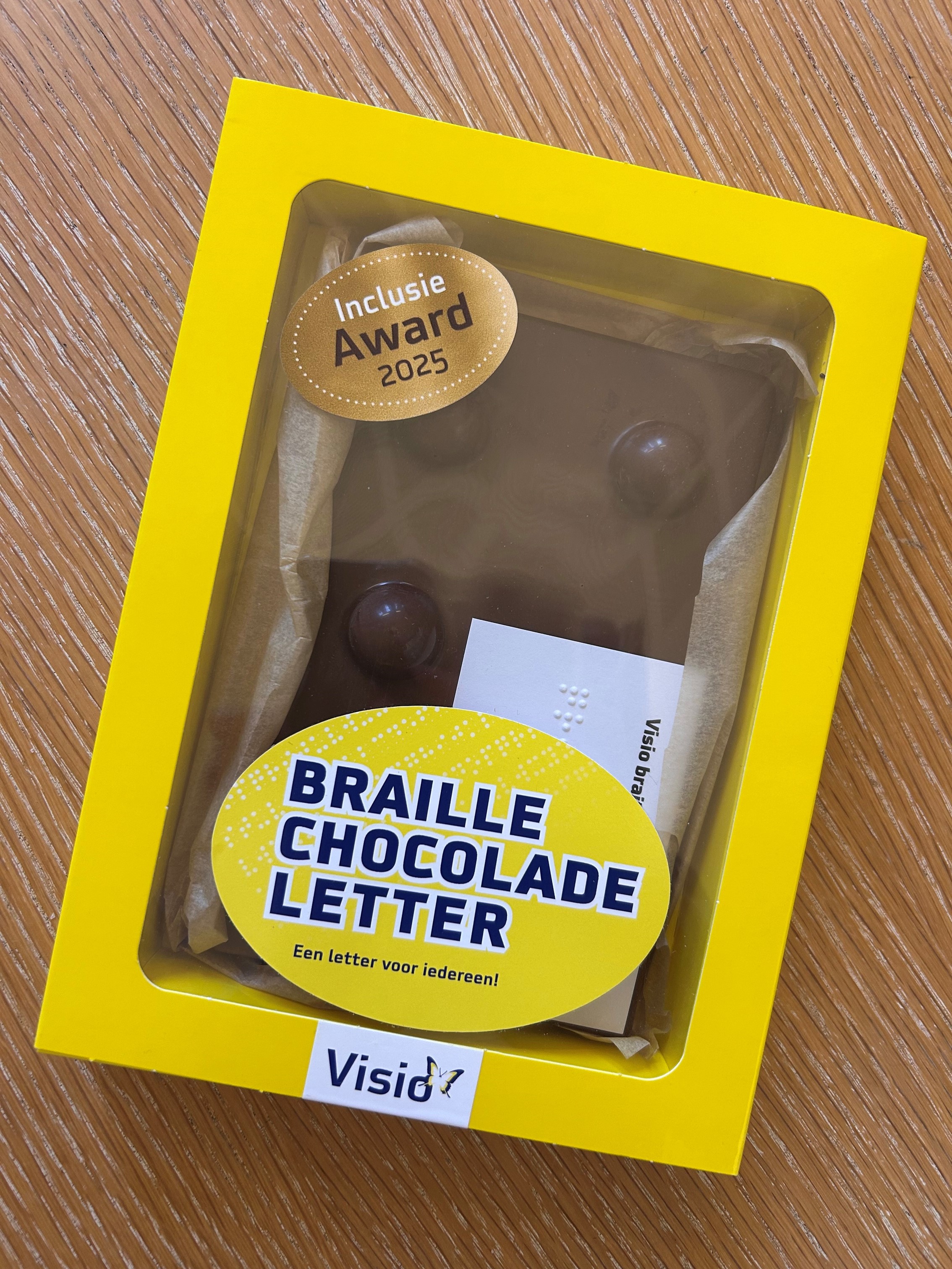 Afbeelding van de braille chocoladeletter. De letter is verpakt in een geel doosje. Er staat een sticker op met "Inlcusie Award 2025".