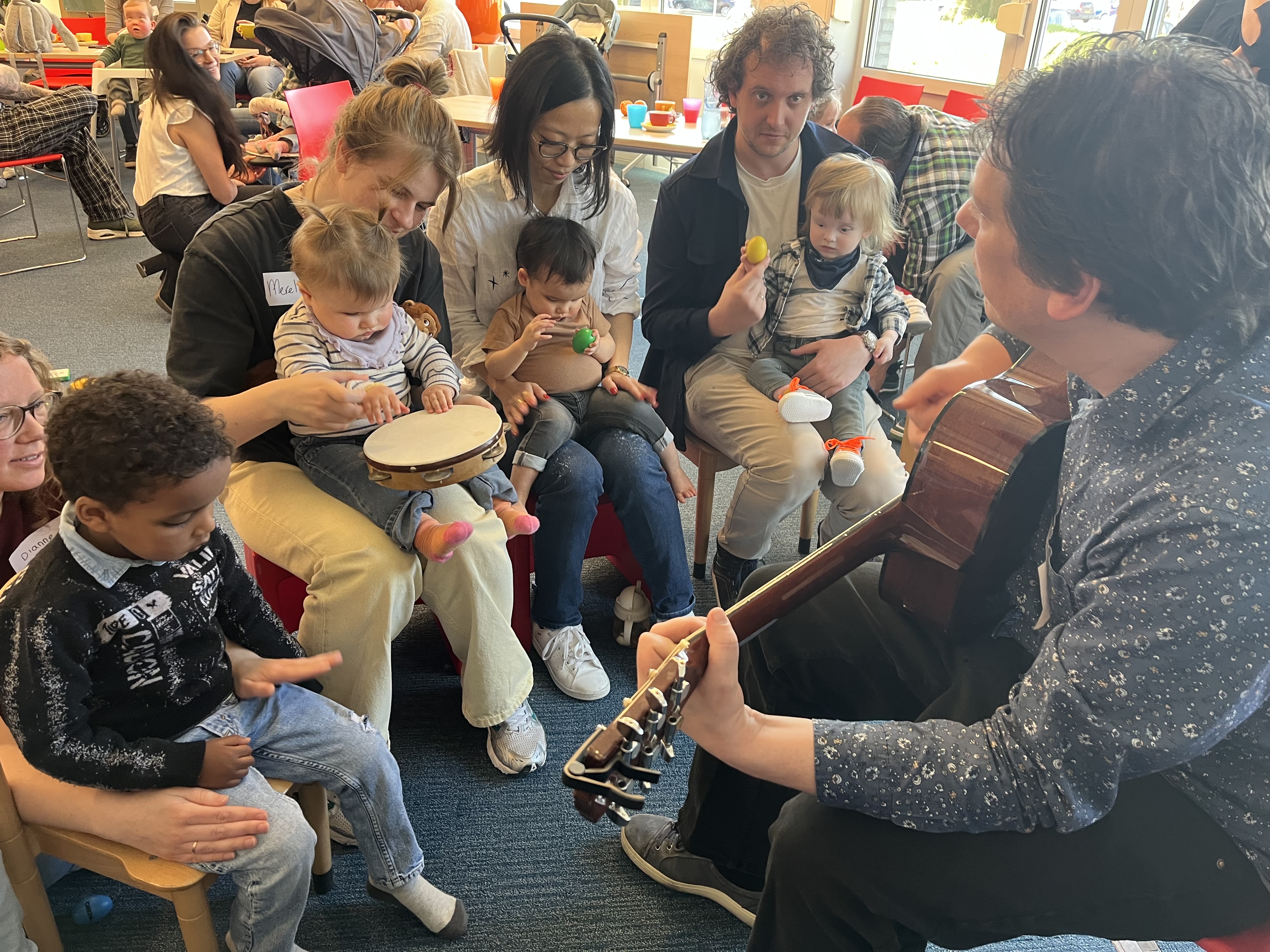 Ouders en blinde, jonge kinderen zitten samen rondom een muziekdocent die gitaar speelt
