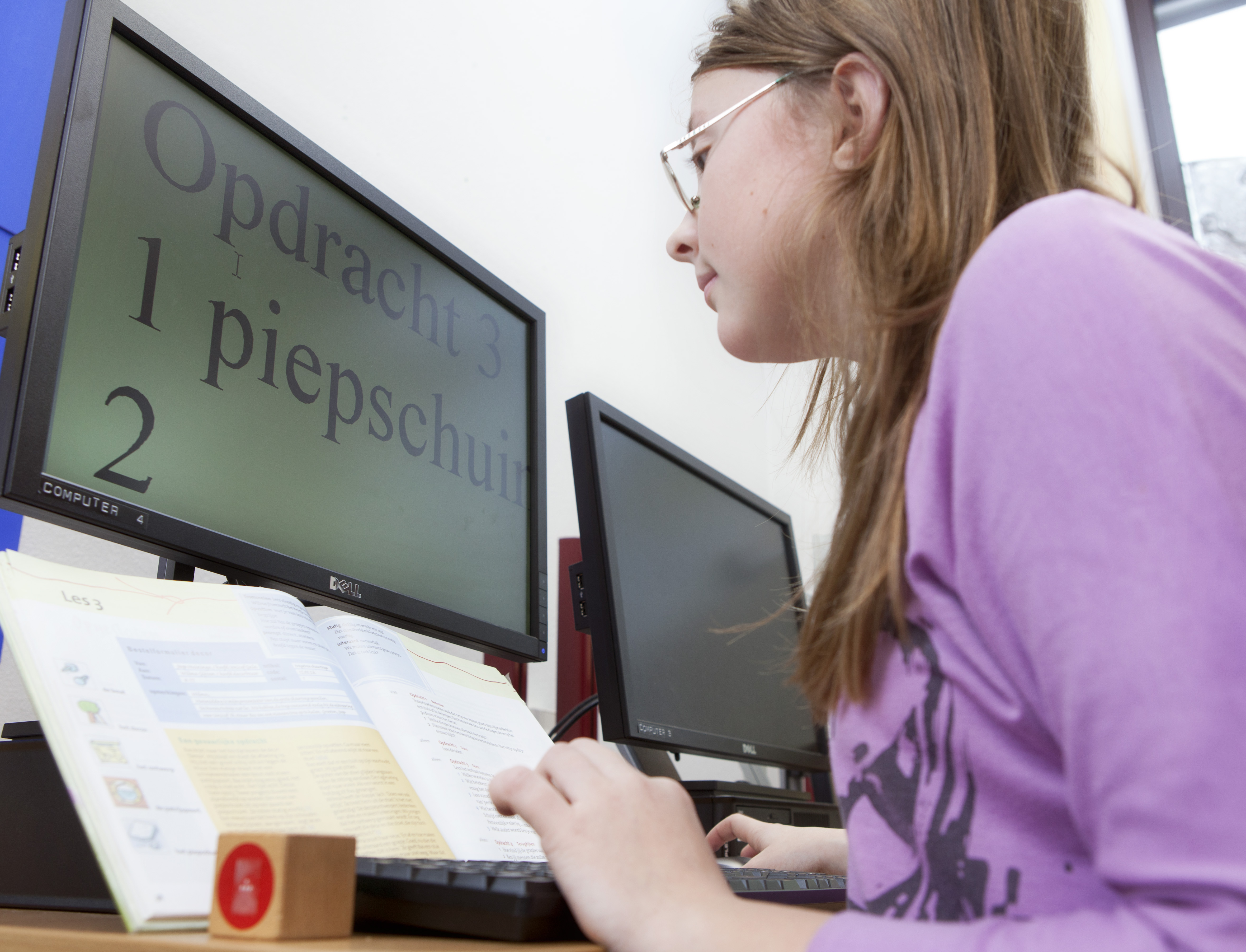 Leerlinge met visuele beperking werkt aan schoolopdracht op een beeldscherm met behulp van toegankelijkheidssoftware