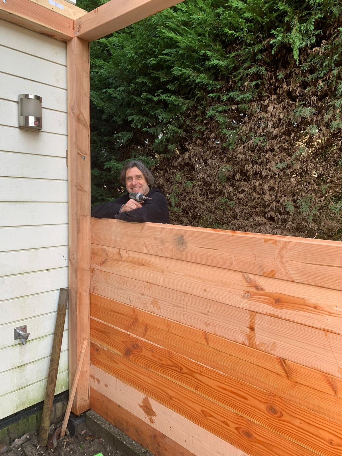 Frank leunt op de zijkant van de pergola in aanbouw Frank leunt op de zijkant van de pergola in aanbouw